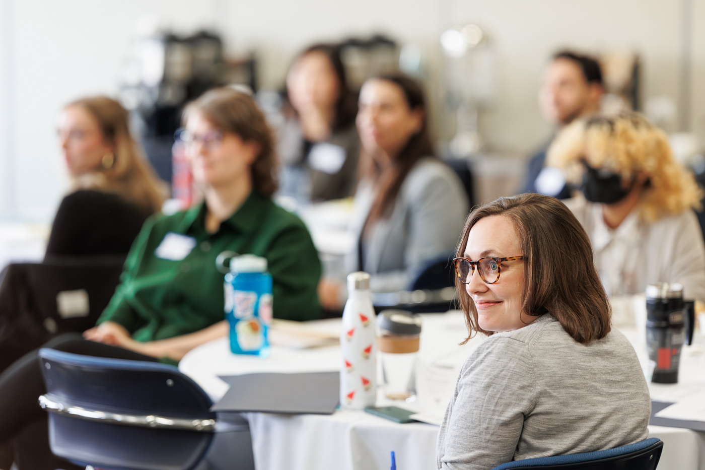 A group of individuals around a table listening to a presentation at an event